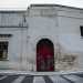 La struttura presenta al centro un arco in pietra che racchiude il rosso portone di ingresso serrato da un lucchetto...